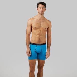 A man stands wearing blue boxer briefs with a black waistband.