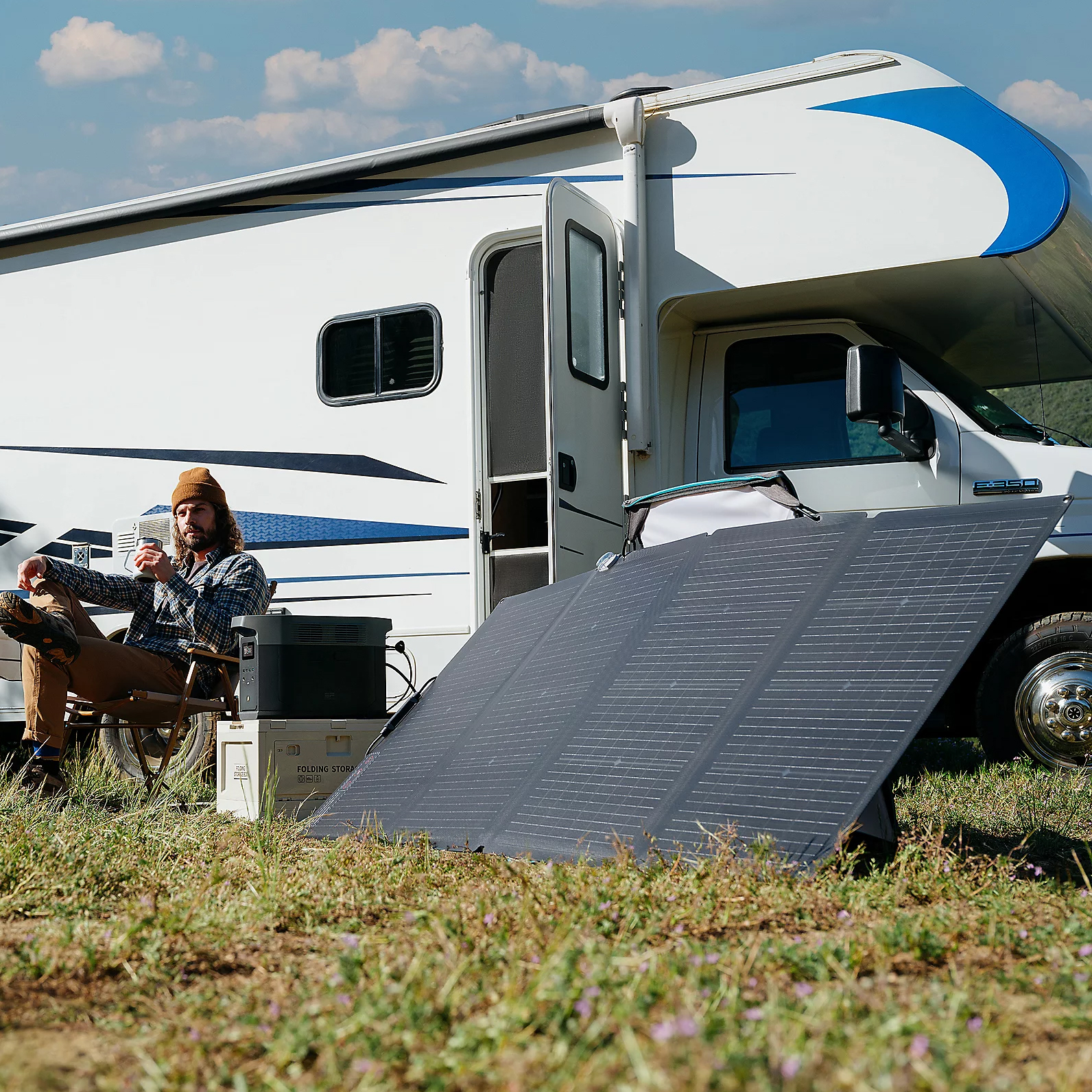 A person relaxes next to a motorhome with a portable solar panel and a power station on the ground.