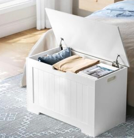 White storage bench with an open lid, revealing blankets and magazines inside.