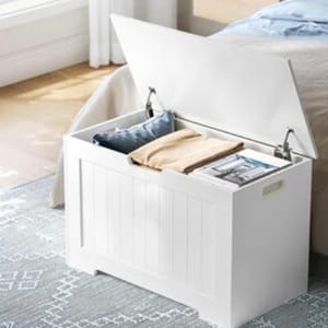 White storage bench with an open lid, revealing blankets and magazines inside.