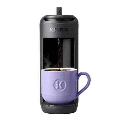 A Keurig coffee maker brews coffee into a purple mug.