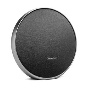 A sleek, circular Harman Kardon wireless speaker with a black fabric front and metallic rim, designed for stylish audio output.