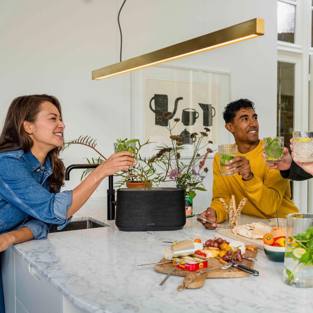 A black Harman Kardon smart speaker with a cylindrical shape is placed on a kitchen countertop.