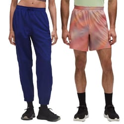 A person is wearing blue jogger pants with black sneakers, while another wears multicolored pink and orange shorts with black socks and sneakers.