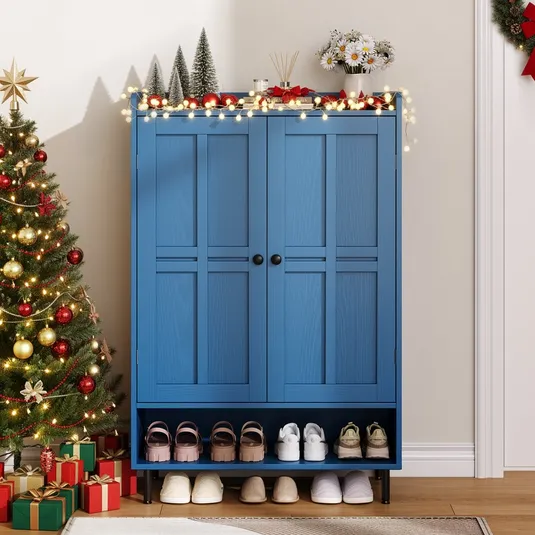 A blue shoe cabinet with decorative lights, mini trees, and flowers on top is next to a Christmas tree with ornaments and gifts. Shoes and slippers are neatly arranged below the cabinet.