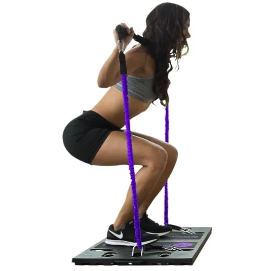 A woman exercises on a resistance band training platform, performing a squat while holding handles attached to purple resistance bands.