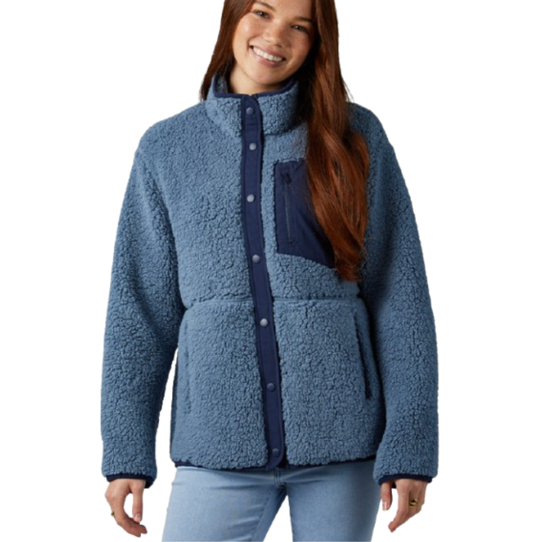 Blue fleece jacket with a high collar, snap button closure, and a contrasting navy chest pocket, paired with light blue jeans.