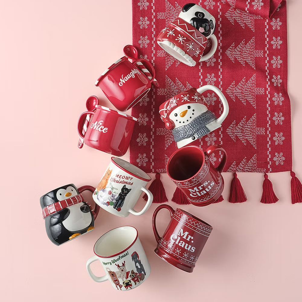 A collection of various Christmas-themed mugs with festive designs and text like \“Naughty,\“ \“Nice,\“ and \“Meowy Christmas.\“