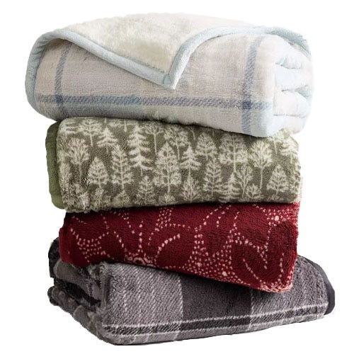 A stack of four plush blankets with different patterns: a light plaid, green with trees, red with leaves, and a dark plaid.