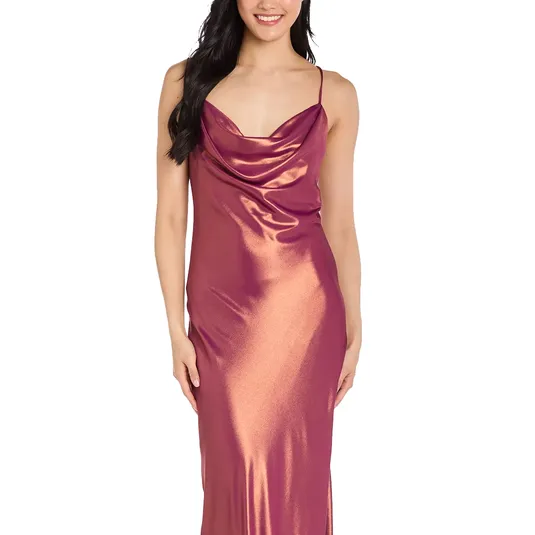 A woman wears a shimmering, satin-like, sleeveless gown in a copper-pink hue with a draped cowl neckline and thin straps.