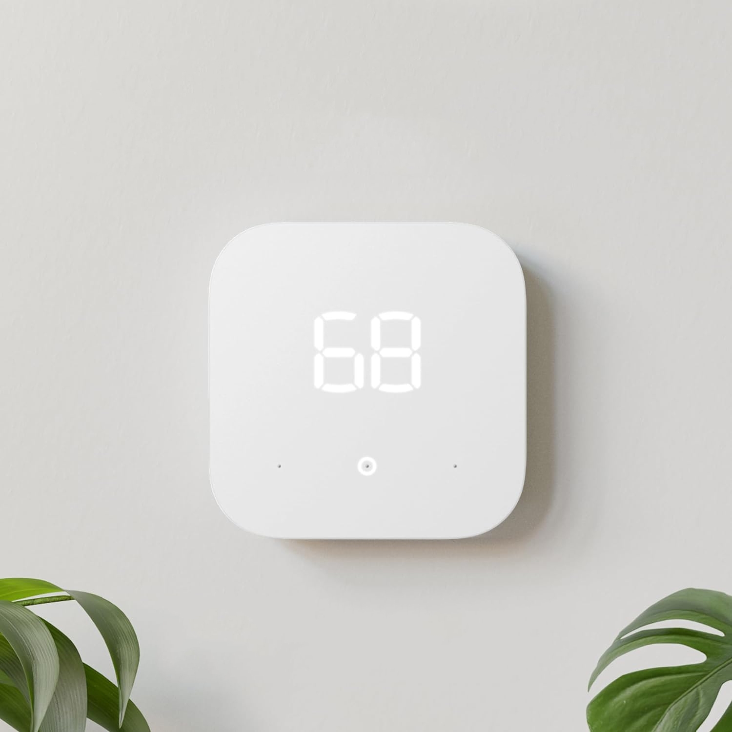 White square digital thermostat displaying a temperature of 68 degrees, mounted on a wall near a green plant leaf.