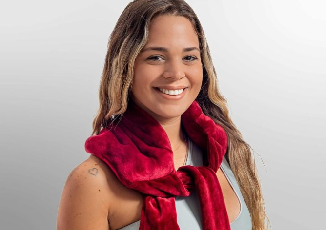 A smiling person is wearing a red plush scarf, with a small heart tattoo visible on their left shoulder.
