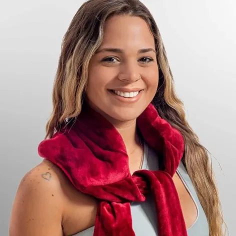 A smiling person is wearing a red plush scarf, with a small heart tattoo visible on their left shoulder.