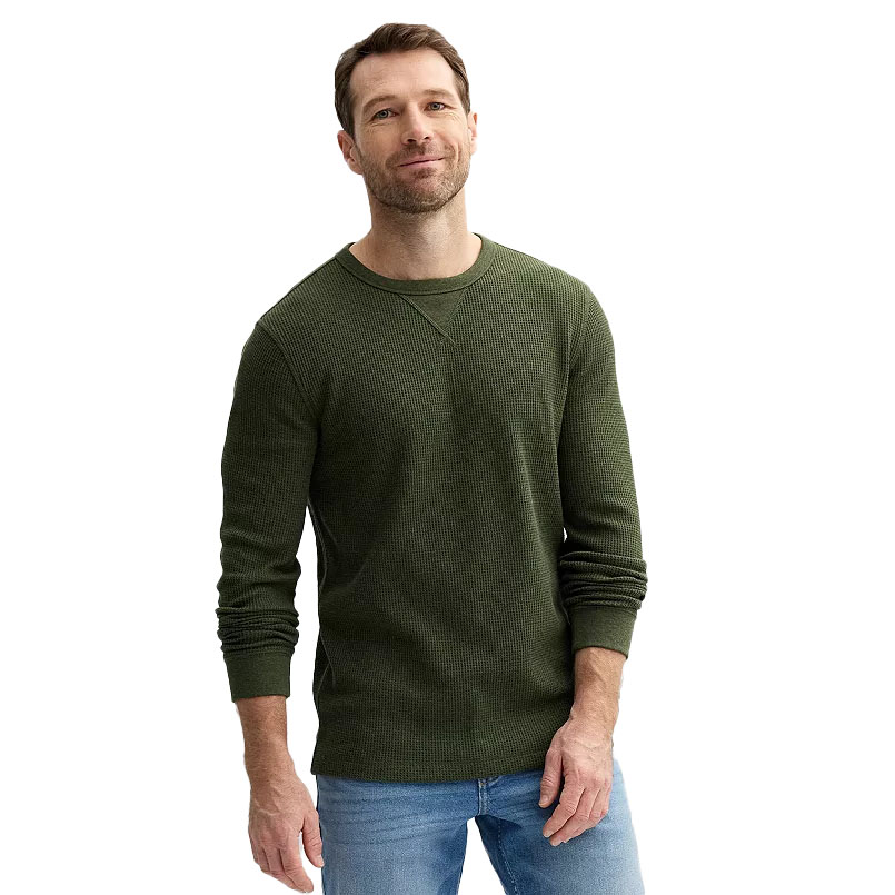 A man is wearing a green waffle-texture long-sleeve shirt paired with light blue jeans, standing against a plain background.