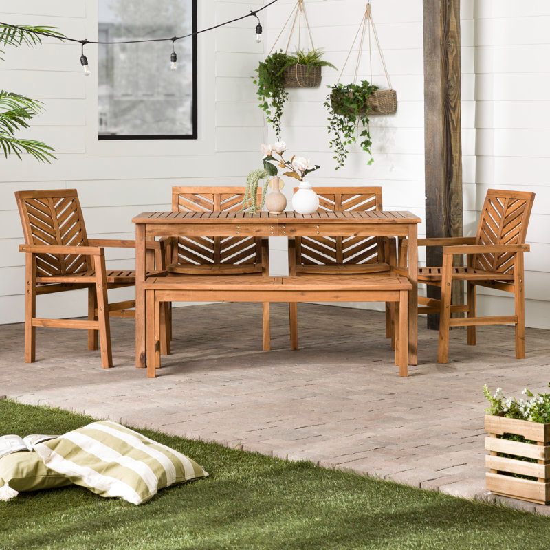 Wooden outdoor dining furniture set with one table, four chairs, and a bench on a patio. Decor includes hanging plants and vases on the table.