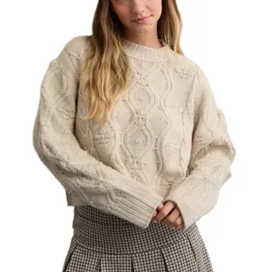 A woman is wearing a cream-colored, cable-knit sweater with ribbed cuffs and a pleated houndstooth skirt.