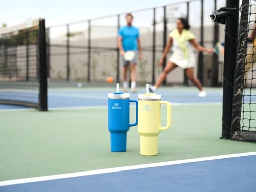 Two insulated hydration bottles, blue and yellow, with carrying handles and straws, are positioned on a tennis court.
