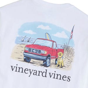 A white Vineyard Vines shirt features an illustration of a red pickup truck with a surfboard, a dog, and an American flag on a beach with sailboats in the background.