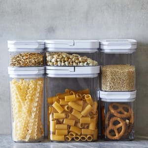 A 20-piece dry food storage set featuring transparent, airtight containers with white lids, organized neatly with contents like pasta, grains, snacks, and seeds visible inside.