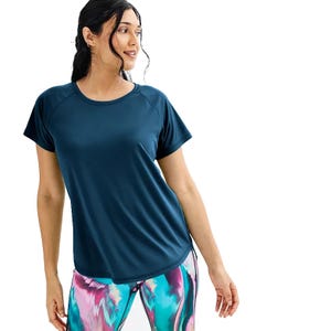 A woman wears a blue Tek Gear Performance Dry Tek Tee with short sleeves and a round neckline, paired with colorful abstract-patterned leggings.