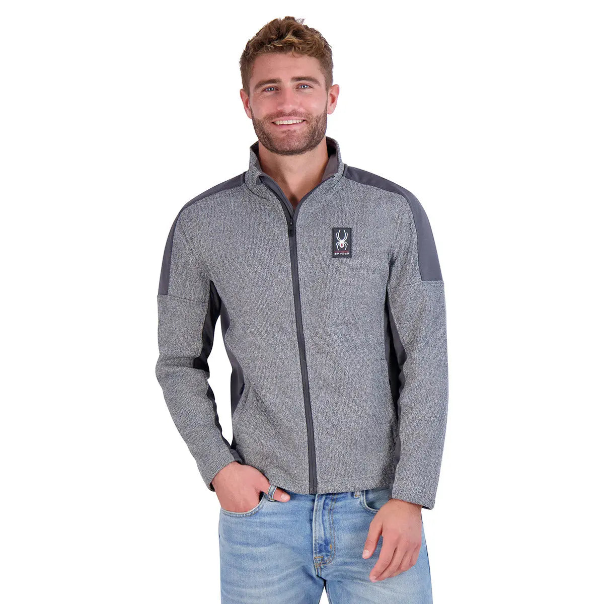 Spyder Men's Mendoza Pullover is a gray zip-up fleece with dark gray shoulder and arm accents, featuring the Spyder logo on the chest. It is paired with light blue jeans and designed for comfort and style.