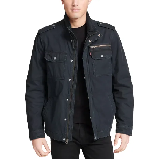 A man is wearing a dark colored field jacket with multiple pockets, snap buttons, and a zippered chest pocket.