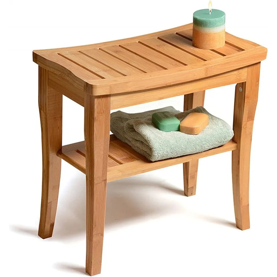 A bamboo bench with a curved slatted top and lower shelf, holding a candle, folded towel, and two soap bars.
