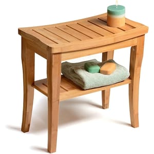 A bamboo bench with a curved slatted top and lower shelf, holding a candle, folded towel, and two soap bars.