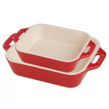 Two red ceramic baking dishes with cream interiors, one smaller and placed on top of the larger one.