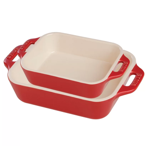 Two red ceramic baking dishes with cream interiors, one smaller and placed on top of the larger one.