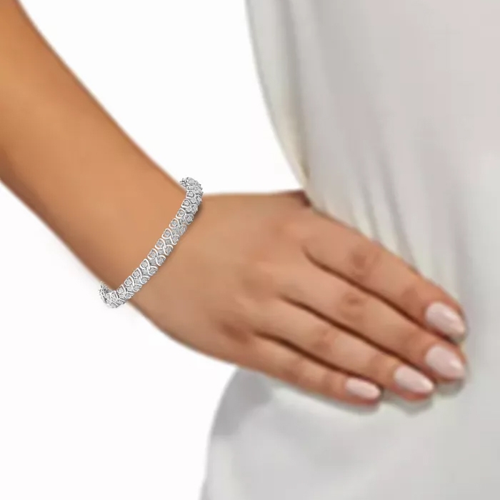A wrist adorned with a silver bracelet featuring a series of intricate, sparkling gemstones in a linked pattern. The arm rests on a white fabric background.
