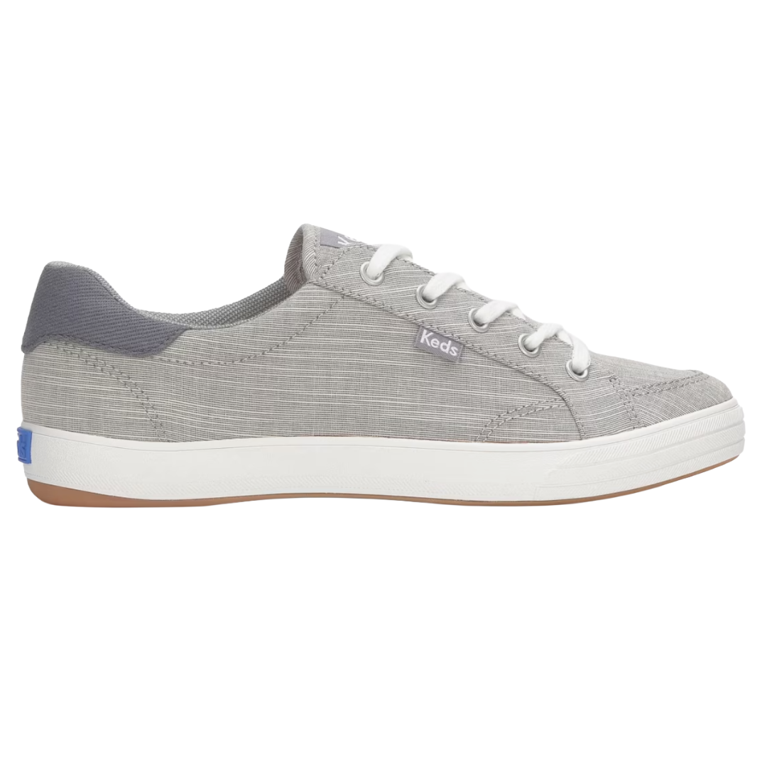 A gray Keds sneaker with white laces and a white sole, featuring a textured fabric and a small logo tag on the side.