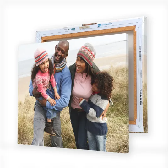 A canvas print displays a family of four enjoying a day at the beach, with two children and two adults wearing winter clothing, smiling and embracing each other.
