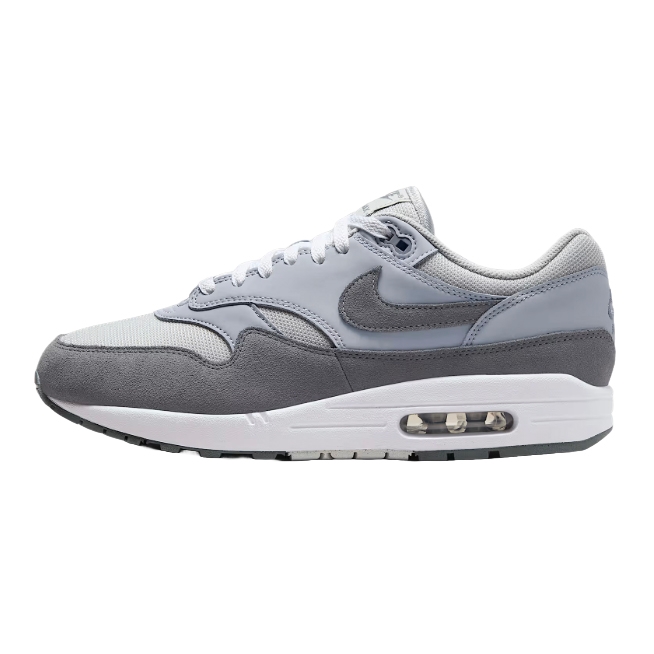 Nike Air Max 1 shoes in grey and white, featuring a suede and mesh upper with a signature visible air unit in the midsole. The design includes a grey Swoosh logo on the side.