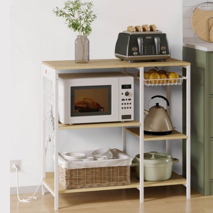 A kitchen rack holds a microwave, black toaster with toast, kettle, fruit basket, and ceramic pot. A wicker basket with dishes sits on the lower shelf, and a vase with flowers decorates the top.