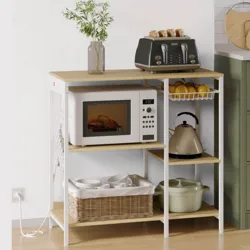 A kitchen rack holds a microwave, black toaster with toast, kettle, fruit basket, and ceramic pot. A wicker basket with dishes sits on the lower shelf, and a vase with flowers decorates the top.