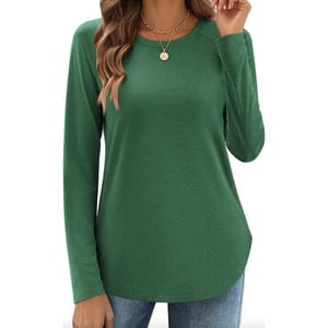 A woman is wearing a long-sleeve, green crew neck top with a rounded hem. She is accessorizing with a gold necklace and blue jeans.