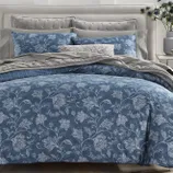 A bedding set featuring a blue floral pattern includes pillows and a comforter on a tufted headboard bed, complemented by grey accents and a decorative cushion.