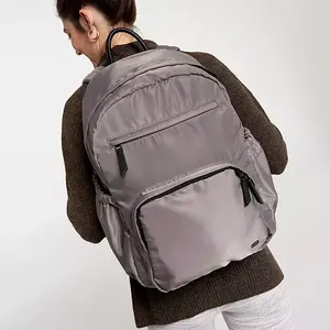 A woman is wearing a gray Calia work backpack featuring multiple zippered compartments and a sleek fabric finish.