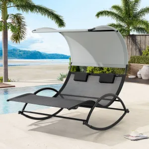 A two-person outdoor rocking chaise lounge with a sunshade canopy beside a pool, surrounded by palm trees and a beach view.