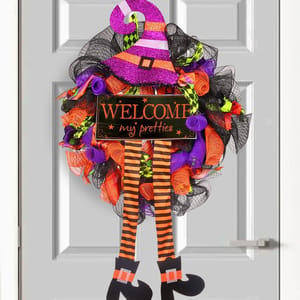 A colorful Halloween wreath featuring a witch's hat, striped legs, and a sign reading \“Welcome my pretties.\“ The design includes black, orange, purple, and green mesh and ribbons.