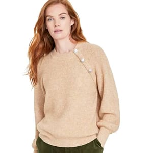 A beige knit sweater featuring plush fabric and decorative jeweled buttons along the shoulder seam, paired with green pants.