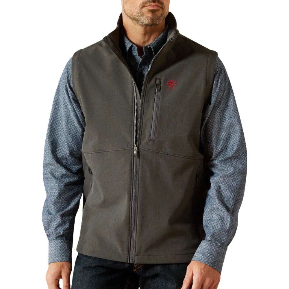 A man is wearing a gray zip-up vest over a long-sleeve blue patterned shirt. The vest features a small red logo on the chest and has zippered pockets.