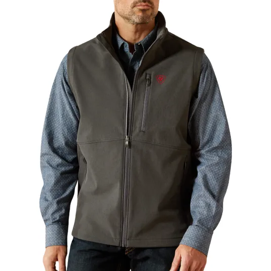 A man is wearing a gray zip-up vest over a long-sleeve blue patterned shirt. The vest features a small red logo on the chest and has zippered pockets.