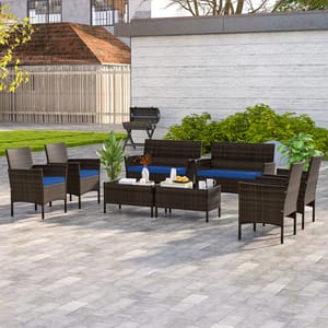 8-piece patio set includes two loveseats, four armchairs, and two coffee tables, all in dark wicker with blue cushions. Ideal for outdoor settings such as patios or gardens, featuring a simple and modern design with scattered greenery and a grill backdrop.