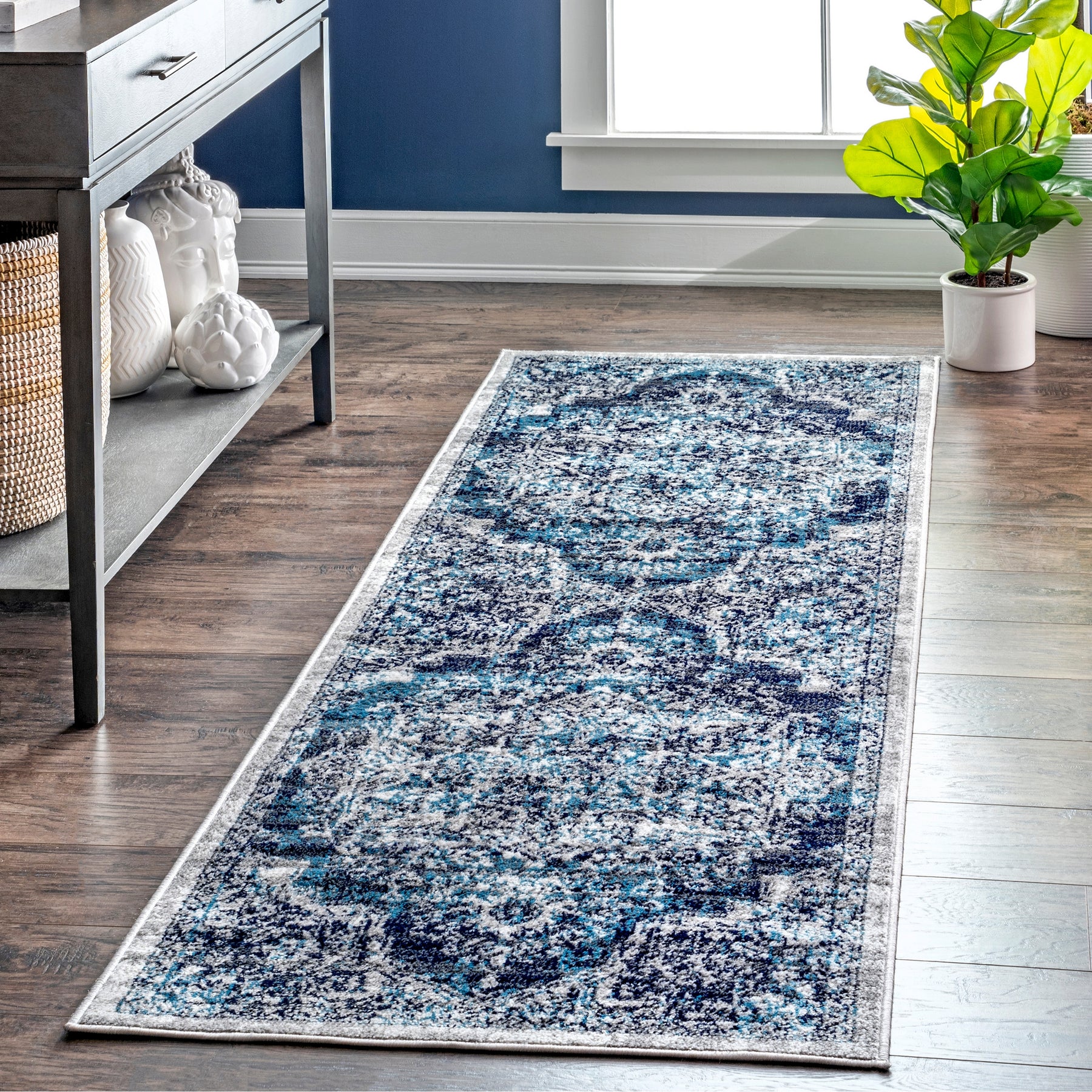 A blue and white patterned runner rug on a wooden floor, placed next to a console table with decorative items and a potted plant.