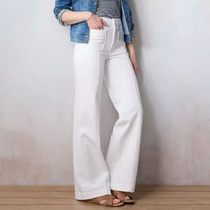 A person wearing white wide-leg pants, a striped shirt, denim jacket, and tan sandals.