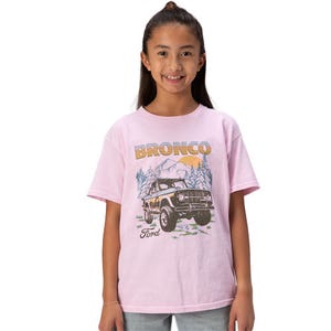 A child wearing a pink T-shirt featuring a vintage Ford Bronco graphic with mountains in the background.