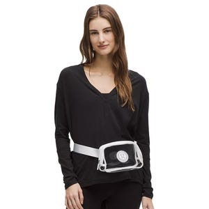 A person wearing a black long-sleeve top and black pants, with a transparent belt bag featuring a logo, worn around the waist.