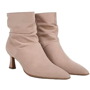 A pair of beige, mid-heel, pointed-toe ankle boots with a slouched design.